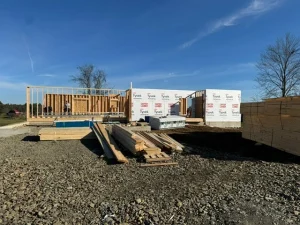 A house under construction with a wood frame on a gravel ground. The walls are covered in white Tyvek wrap.